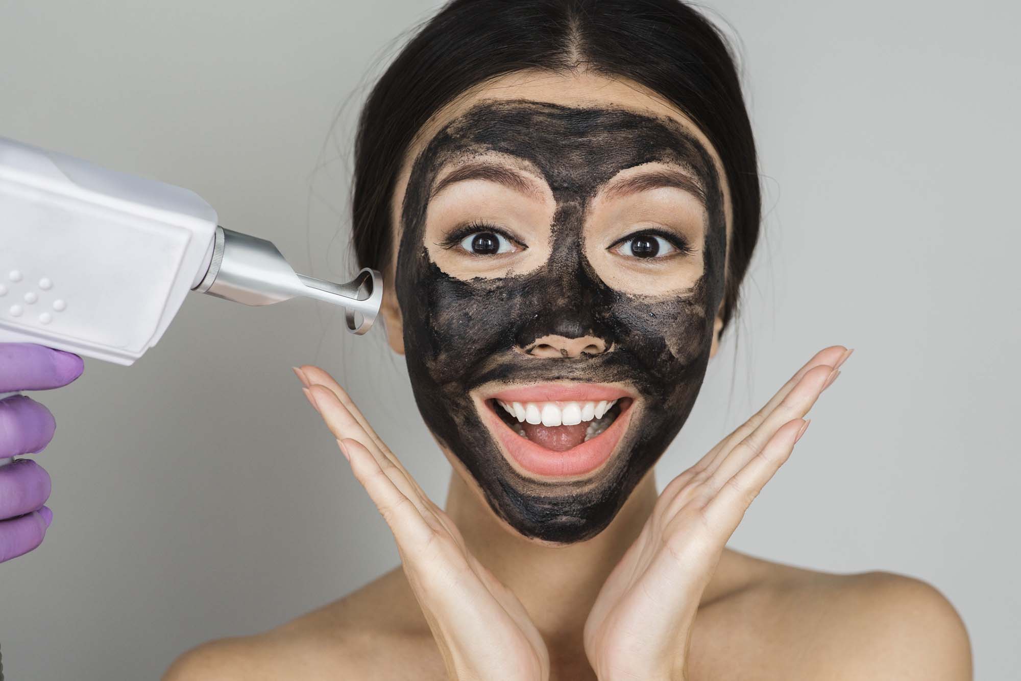 Asian woman with black mask on face with surprised emotionon, advertising procedure of carbon peel Asian woman with black mask on face with surprised emotionon, advertising procedure of carbon peel
