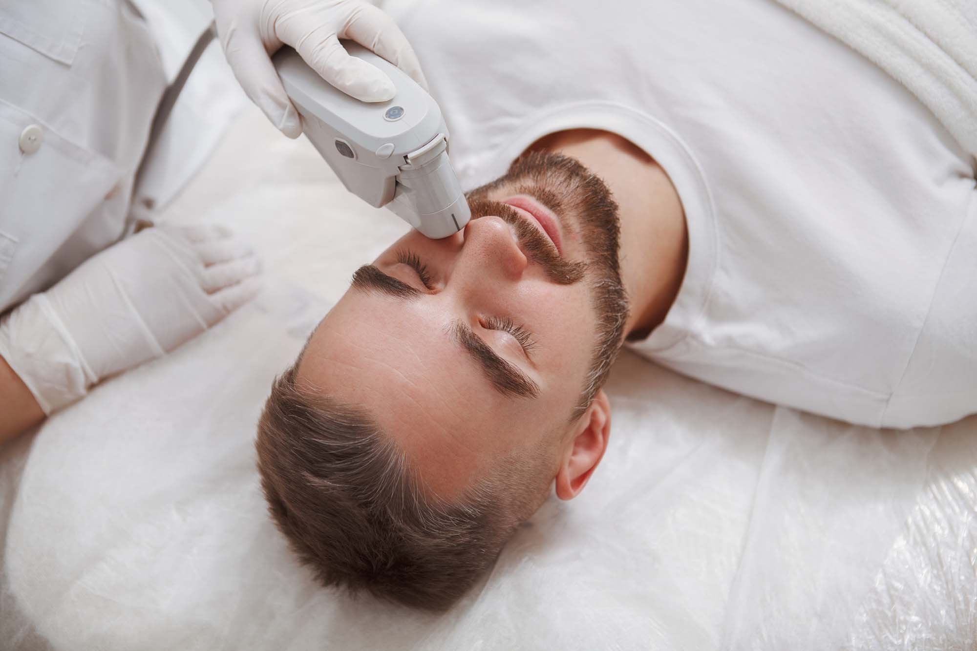 Handsome man getting facial skincare treatment at salon Close up of a bearded man enjoying getting laser facial treatment by professional cosmetologist